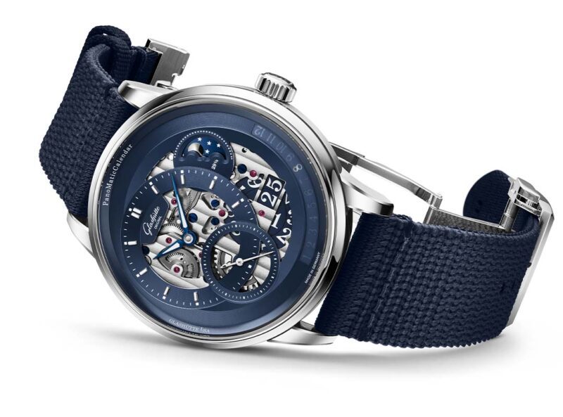 A luxury Glashütte Original wristwatch with a blue textile strap, exposed gears and mechanical components, and a blue openwork dial featuring multiple sub-dials—a stunning addition to the PanoMaticCalendar collection.