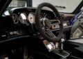 Close-up of a Gunther Werks remastering, highlighting a Porsche 911 interior with a black suede steering wheel, analog gauges, manual gear shifter, and carbon fiber trim.
