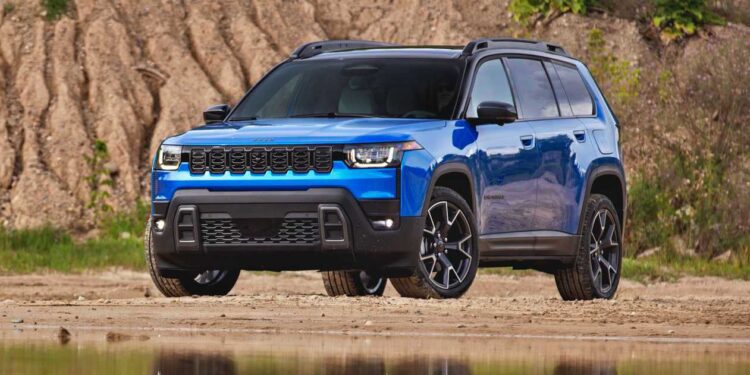 A blue SUV, possibly the 2026 Jeep Cherokee First Look: Rugged Design Hybrid Power and More Space, is parked on a sandy surface near water, with grass and soil mounds in the background.