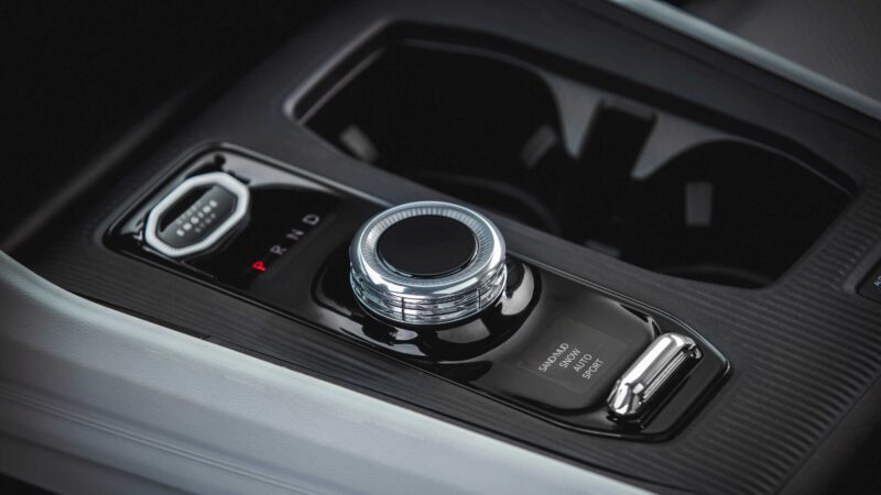 Close-up of the 2026 Jeep Cherokee center console, featuring a rotary gear selector, cup holders, and drive mode buttons labeled Normal, Eco, and Sport—highlighting its rugged design and hybrid power.