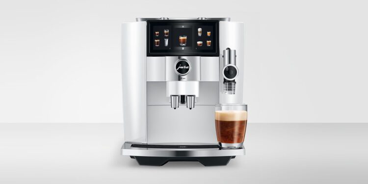 A Diamond White JURA J8 Twin automatic coffee machine with a digital display, dispensing coffee into a clear glass filled with a beautifully layered espresso drink.