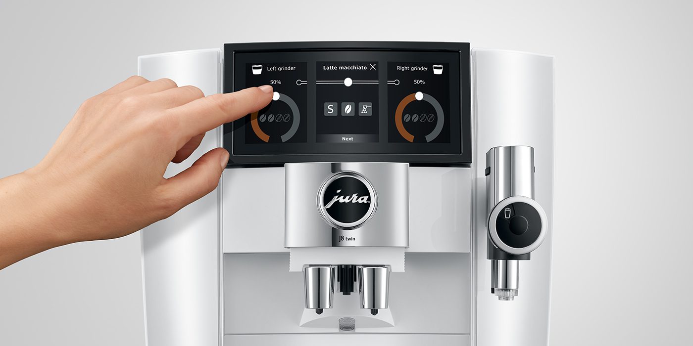 A hand adjusts settings on the touchscreen display of the JURA J8 Twin coffee machine in elegant Diamond White, with options for left and right grinders visible.