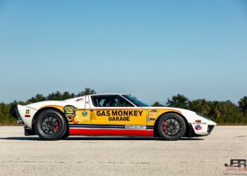 A yellow and white Ford GT sports car, known as the BADD GT and driven by Jonny Bohmer, with "Gas Monkey Garage" branding, is parked on a paved surface under a clear sky.