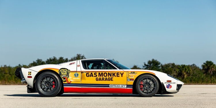 A yellow and white Ford GT sports car, known as the BADD GT and driven by Jonny Bohmer, with "Gas Monkey Garage" branding, is parked on a paved surface under a clear sky.