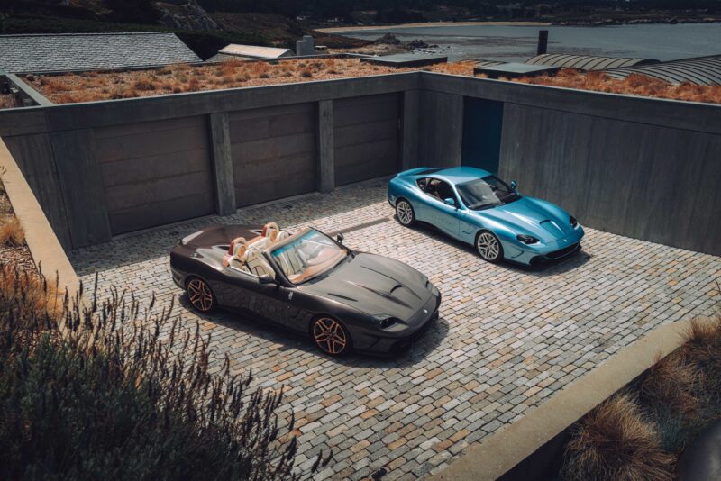 Two sports cars, one gray convertible and one blue coupe, are parked on a stone driveway inside a modern concrete garage—inside SOC’s Monterey Debut featuring Convoys Exclusives and Touring's Veloce12 Barchetta Reveal.