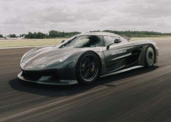 A grey Koenigsegg Jesko Absolut with "World Record Car" text on the door speeds along a racetrack, set against a grassy landscape and cloudy sky, reflecting its 0-250-0 MPH world record capabilities.