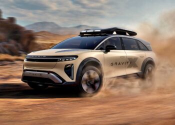 A beige Lucid Gravity SUV with a roof box drives off-road, kicking up dust in a desert landscape—echoing the trail-ready spirit of the Pebble Beach Debut: Rugged Lucid Gravity X Concept with 828 HP and adventure-focused upgrades.