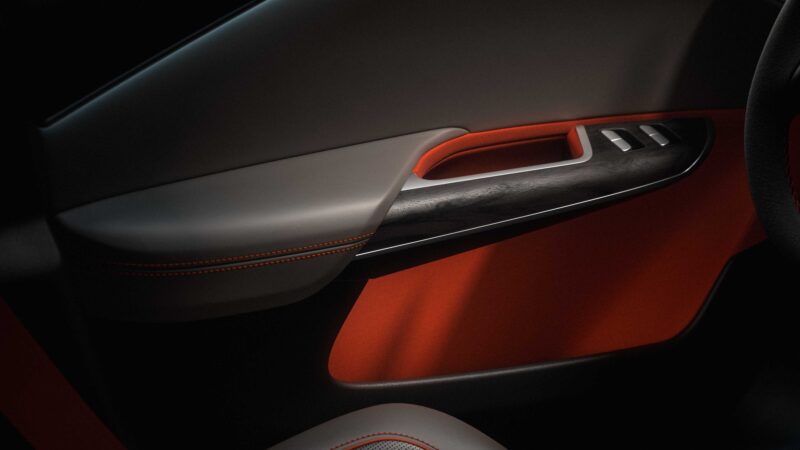 Close-up of a car door interior featuring the armrest, window controls, red accent stitching, and dark wood trim—reflecting the premium details seen in the Pebble Beach Debut: Rugged Lucid Gravity X Concept with 828 HP & trail-ready upgrades.