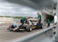 Two people inspect a black vintage Lotus Type 79 Formula 1 car with John Player Special and Olympus branding, once driven by Jan Lammers, on a racetrack.