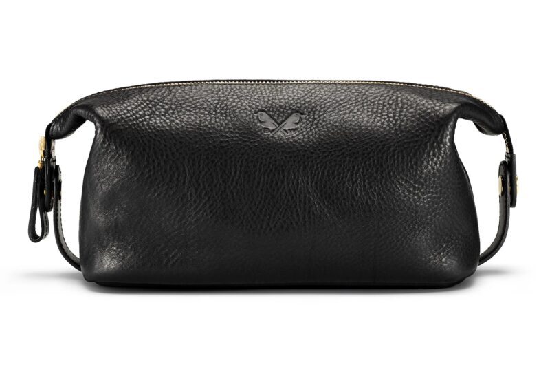 A black leather dopp kit with a pebbled texture, featuring a zipper closure and a small embossed butterfly logo on the front—perfect for those seeking luxury accessories and timeless style.