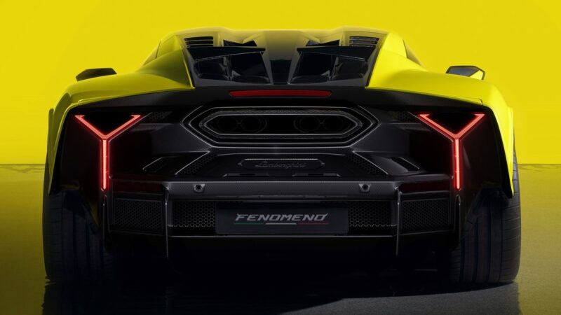A rear view of the Lamborghini Fenomeno: Limited-Run V12 Masterpiece Unveiled at Monterey, showcasing its yellow finish, Y-shaped LED tail lights, prominent exhausts, and a "Fenomeno" plate against a striking yellow background.