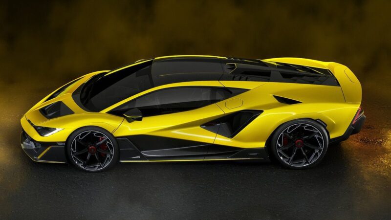 A yellow Lamborghini Fenomeno: Limited-Run V12 Masterpiece Unveiled at Monterey, with black accents, is parked on a dark surface, shown from the side with dramatic lighting and a blurred dark background.