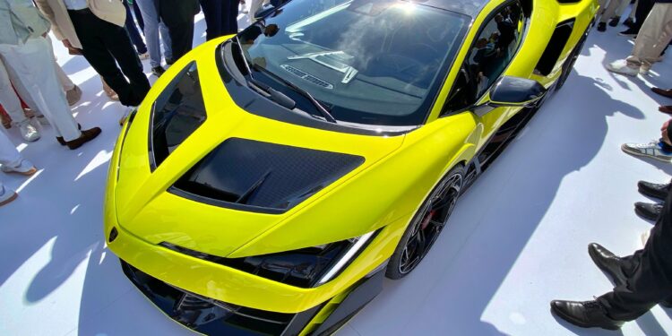 A bright yellow Lamborghini V12 sports car on display, surrounded by a crowd of people, viewed from above—a true collector’s dream.