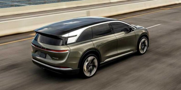 A green electric SUV with impressive autonomy drives on a highway next to the ocean under a partly cloudy sky.