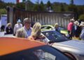 A group of people stand and converse around several parked luxury cars, including a Bentley and the EXP 15 Concept, at an outdoor event during Monterey Car Week on a sunny day.