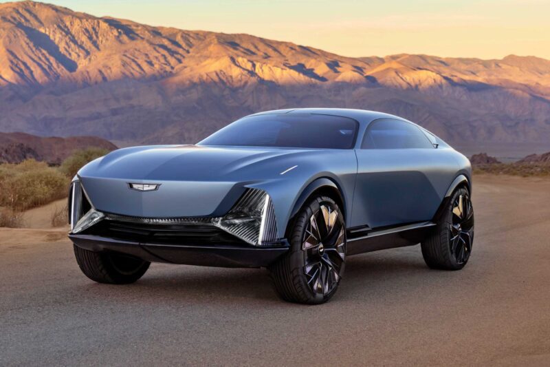 A sleek, futuristic electric SUV—Cadillac Elevated Velocity Concept Revealed: An Extreme Vision for Future Luxury EVs—features tinted windows and large wheels, parked on a paved road with majestic mountains in the background.