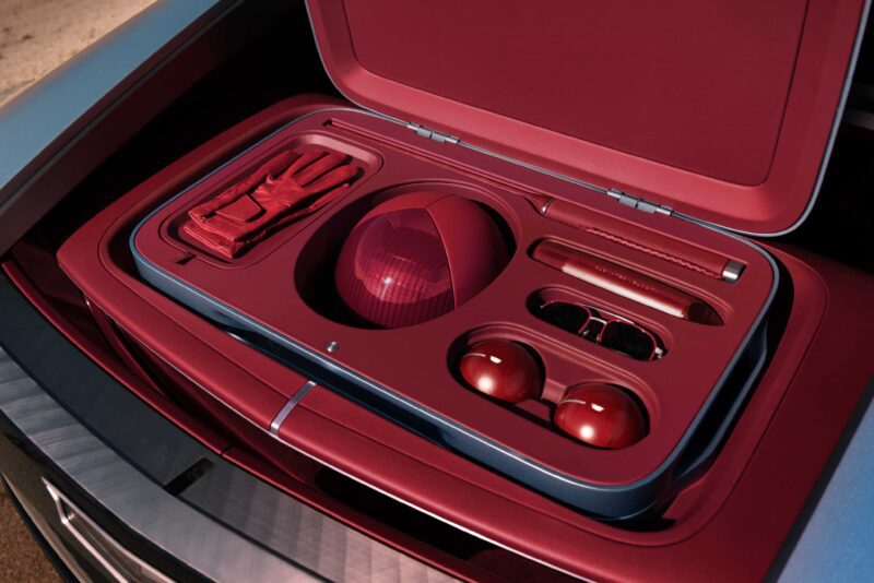 A maroon case, inspired by Cadillac Elevated Velocity concept, containing golf gloves, a golf ball, sunglasses, two smaller balls, a pen, and a cylindrical item—all neatly organized for future luxury EVs enthusiasts.