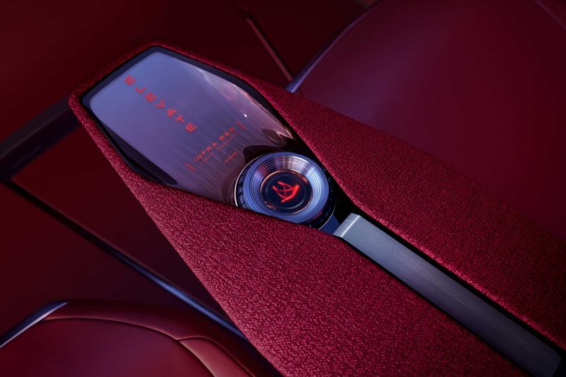 Close-up of a car’s red interior center console featuring a modern control dial and digital display with illuminated text, embodying the advanced design seen in luxury EVs like the Cadillac Elevated Velocity concept.