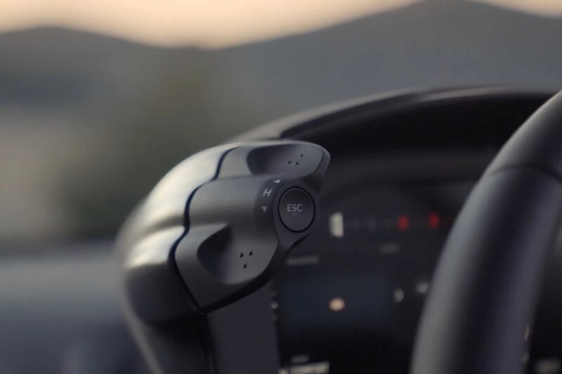 Close-up of a car steering wheel with a visible "ESC" button and directional controls, dashboard blurred—similar to the tech found in the 2025 McLaren Artura Spider Review: Droptop With A Split Personality.