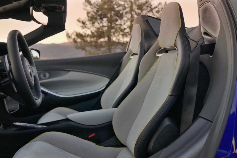 Interior view of a modern sports car with two leather bucket seats, a steering wheel, and a tree visible through the window—perfect for experiencing the 2025 McLaren Artura Spider Review: Droptop With A Split Personality.