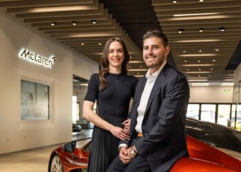 A man and woman pose together inside McLaren Scottsdale, standing in front of an orange sports car, capturing a memorable moment in this Year of Growth.