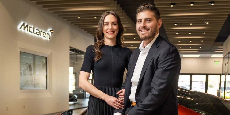 A man and woman pose together inside McLaren Scottsdale, standing in front of an orange sports car, capturing a memorable moment in this Year of Growth.