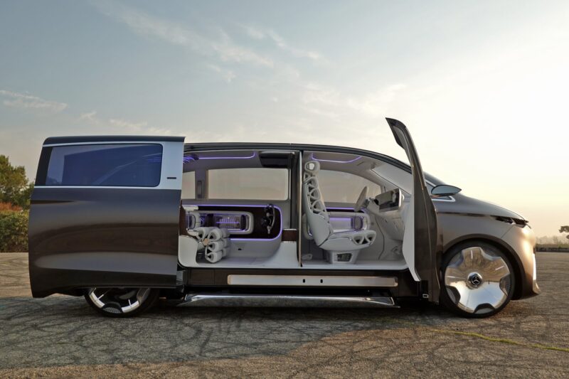 Futuristic van luxury with sliding and open doors, visible interior seating, and ambient lighting—this Mercedes-Benz Vision V concept is shown parked on a paved surface at sunset.