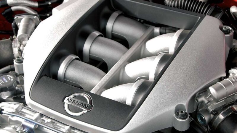 Close-up view of a Nissan R35 GT-R engine cover with prominent intake manifold pipes and the Nissan logo displayed on a central panel—an iconic image marking the end of an era.