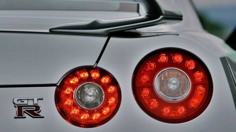 Close-up of the rear of a Nissan R35 GT-R sports car, showcasing the iconic GT-R badge and illuminated circular tail lights—a fitting tribute at the end of an era.