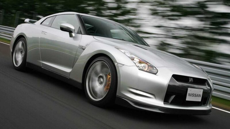 A silver Nissan R35 GT-R sports car driving on a road with blurred trees in the background captures the end of an era—leaving us to wonder what comes next for this iconic machine.
