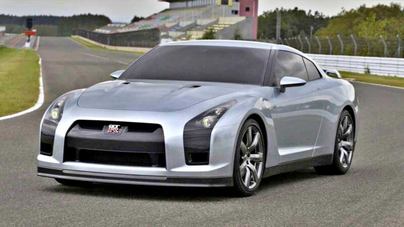 A silver Nissan R35 GT-R sports car is parked on a racetrack at the end of an era, with empty grandstands and trees in the background.