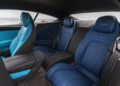 The interior of a luxury Bentley car featuring two blue leather rear seats with quilted detailing and Ombre By Mulliner accents, set against an ocean backdrop.