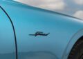 Close-up of a turquoise Bentley’s side panel with the word "Speed" in black script, showcasing its Ombre By Mulliner paint finish, with the wheel and a blurred sky in the background.