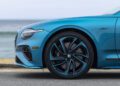 Close-up of the front side of a blue Bentley with a stunning Ombre By Mulliner paint finish, parked near the ocean, highlighting the wheel, fender, and part of the headlight.