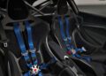 Close-up view of two black racing seats with blue five-point harnesses and a roll cage inside a high-performance car.