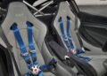 Two grey racing seats with blue multi-point harnesses inside a car, featuring roll cage bars and a minimalist interior design.