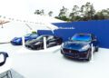 Three Maserati cars, including the striking GT2 Stradale, are displayed on a white platform outdoors, set against a blue Maserati-branded backdrop with a large umbrella partially visible in the foreground.