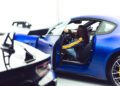 A person sits in the driver’s seat of a blue Maserati with the door open; another black GT2 Stradale is partially visible in the foreground, capturing the excitement of Car Week.