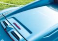 Close-up of a light blue Maserati’s rear engine cover with the red "Cielo" badge, photographed outdoors during Car Week with grass visible in the background.