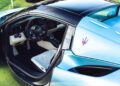 The photo captures the driver’s side interior of a light blue Maserati GT2 Stradale with the door open, showcasing the steering wheel, dashboard, pedals, and Maserati logo—perfect for Car Week enthusiasts.