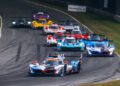 A group of prototype race cars rounding a corner on a racetrack during a motorsport event, with the lead car ahead of the pack.
