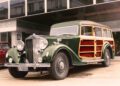 A vintage green and wood-paneled station wagon, reminiscent of the world's greatest artists' classic taste, is parked in front of a modern building.