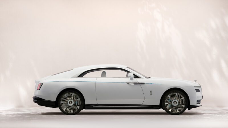 A white Rolls-Royce Bespoke Spectre luxury coupe is shown in profile against a neutral background with subtle light patterns.