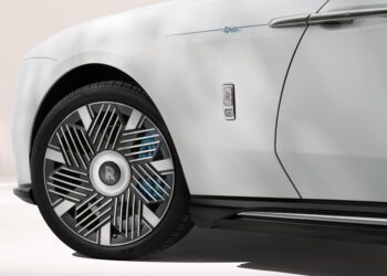 Close-up of a white Rolls-Royce Motor Cars Bespoke Spectre, highlighting the front wheel, unique rim design, and part of the door with a prominent Rolls-Royce badge.