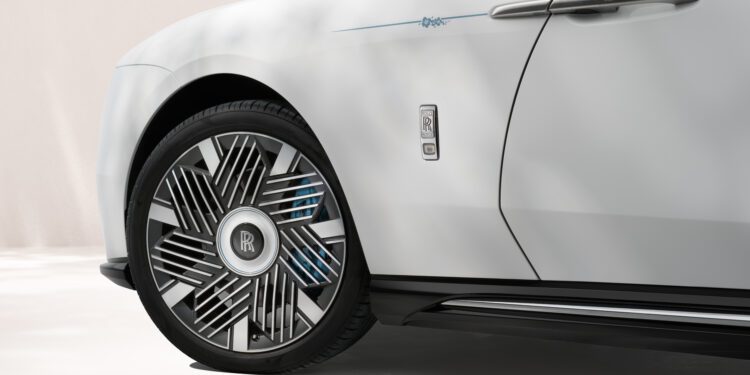 Close-up of a white Rolls-Royce Motor Cars Bespoke Spectre, highlighting the front wheel, unique rim design, and part of the door with a prominent Rolls-Royce badge.