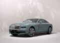 A mint green Bespoke Spectre luxury coupe by Rolls-Royce, with a distinctive grille and stylish alloy wheels, is parked on a light-colored surface against a neutral background.