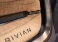 Close-up of a Rivian car door interior featuring a wood panel with the Rivian logo and a small display showing “1 of 1” at Monterey Car Week’s exclusive auction.