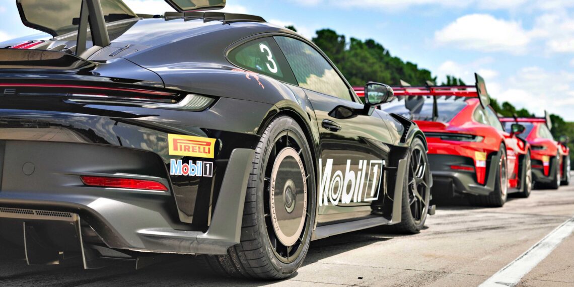 Three race cars with large rear wings, including a Porsche 911 GT3 RS Manthey Package now offered at Porsche Track Experience in Alabama, are lined up on a track, viewed from the rear, featuring Mobil 1 and Pirelli branding.