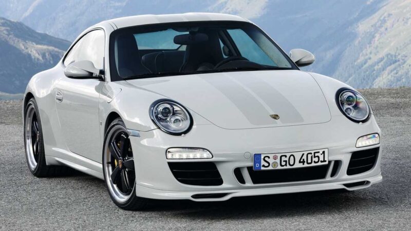 A white Porsche 911 sports car is parked on a paved surface with mountains visible in the background, evoking the spirit of the Porsche 911 Comparison: 997 Sport Classic vs 992 Sport Classic.