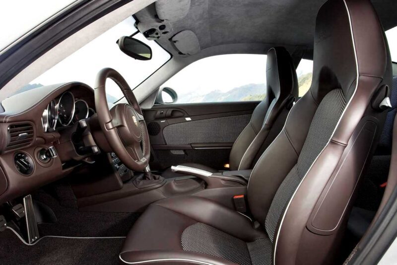 Interior view of a modern sports car, reminiscent of the Porsche 911 Comparison: 997 Sport Classic vs 992 Sport Classic, featuring brown leather seats, a sleek steering wheel, and dashboard controls illuminated by natural light.